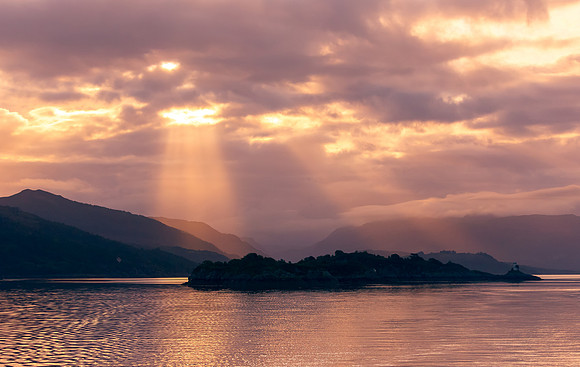 Sunrise in the Inner Hebrides, Scotland, with sunrays bursting through the clouds on the mountain range.  Concept: Tranquility.  Horizontal.  Space for copy.